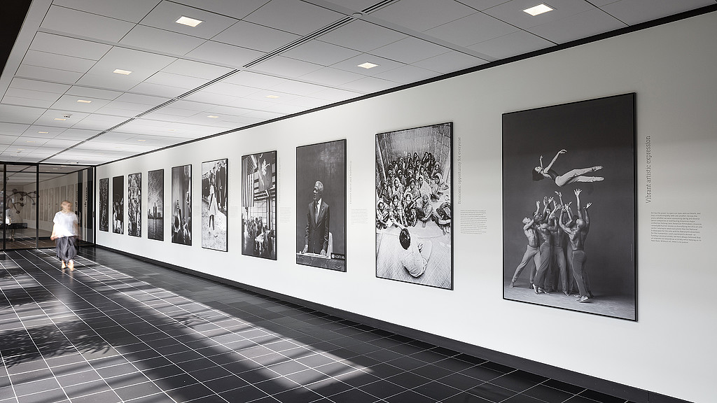 A person walking in a large room with a wall of art.
